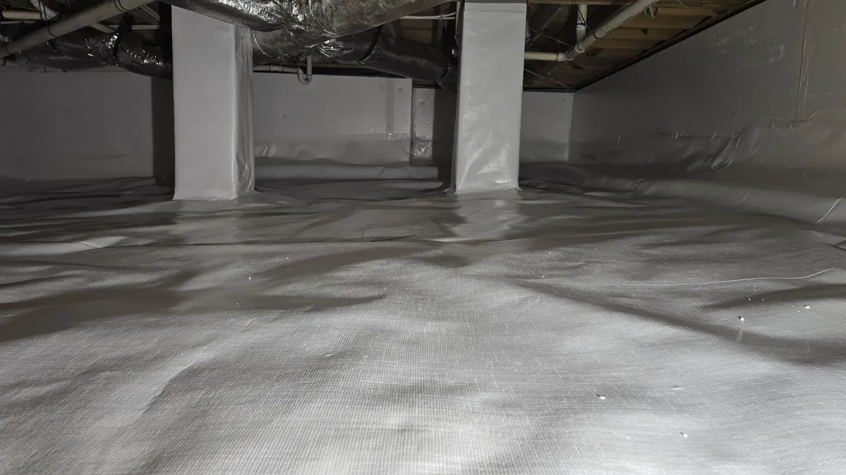 A sealed crawl space with a white vapor barrier covering the floor, the walls, and two support piers under silver ductwork.