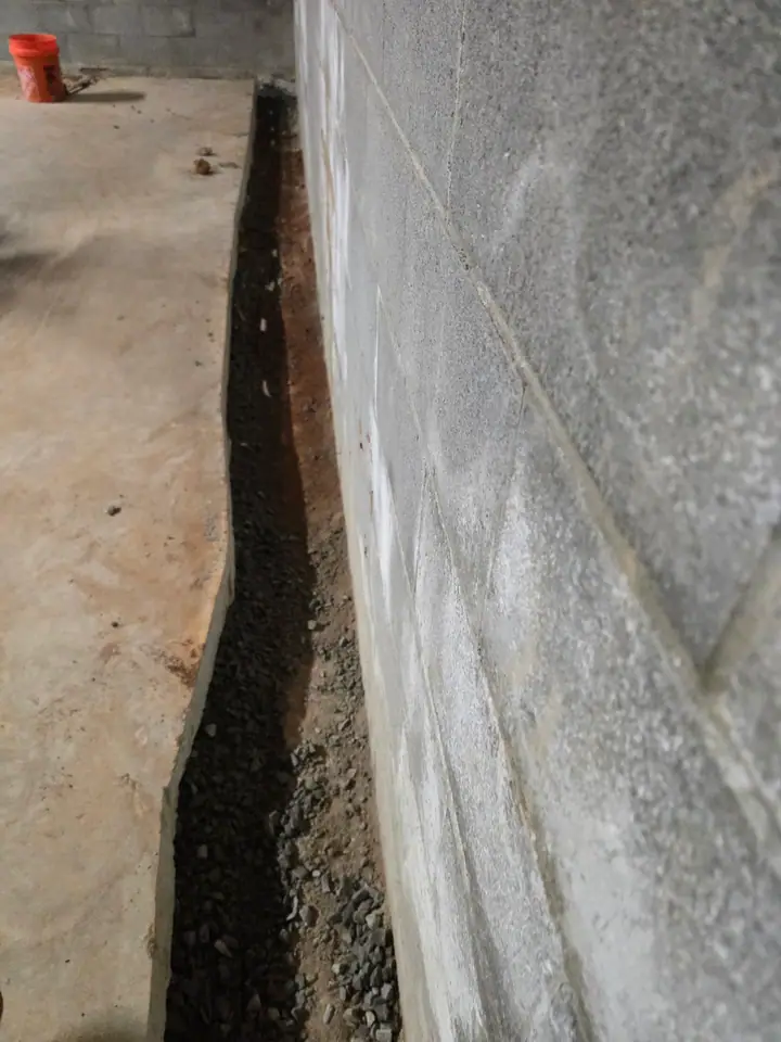 A Rozier Pest Control & Waterproofing crew installing an interior drainage system with gravel in a basement.