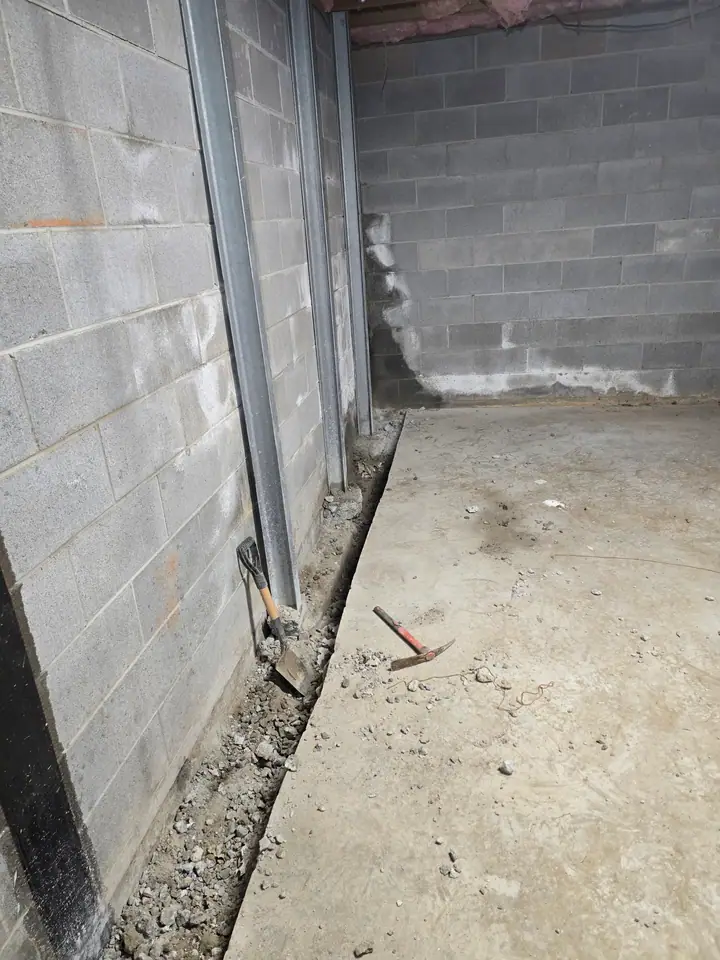A Rozier Pest Control & Waterproofing crew installing an interior drainage system in a basement with visible efflorescence.