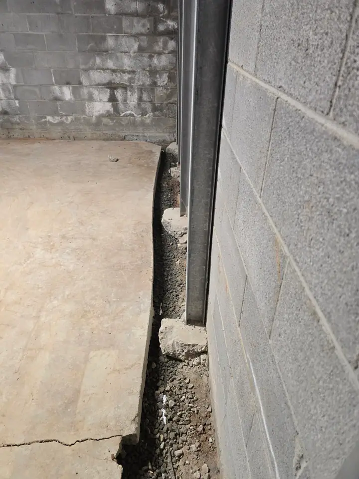 A Rozier Pest Control & Waterproofing crew installing an interior drainage system with steel support beams in a damp basement.