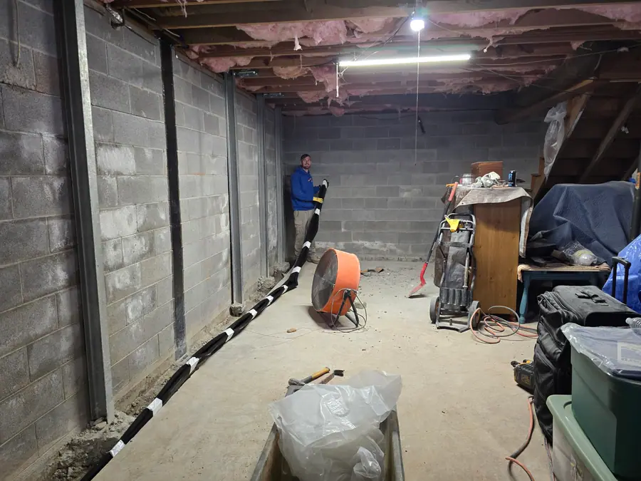 A Rozier Pest Control & Waterproofing technician working on an interior basement drainage system.