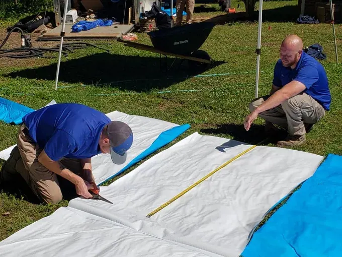 Rozier Pest Control & Waterproofing crew members measuring and cutting vapor barrier on a lawn before an encapsulation.