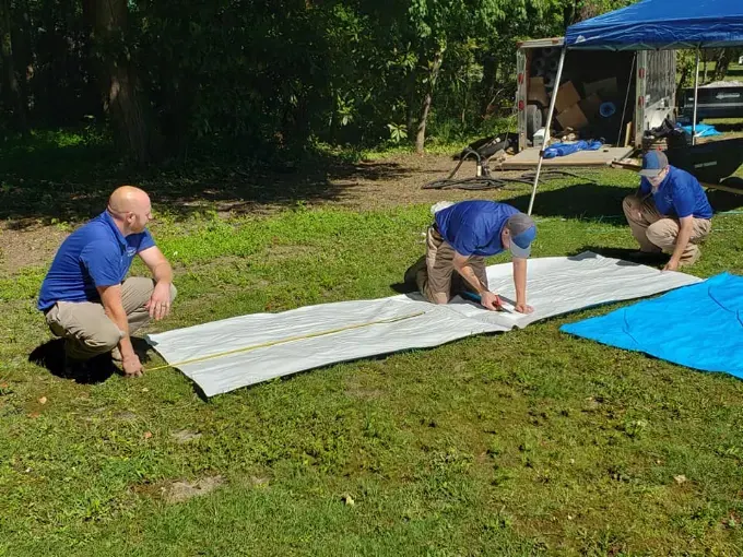 The Rozier Pest Control & Waterproofing crew preparing vapor barrier sheets in a yard beside the job trailer.