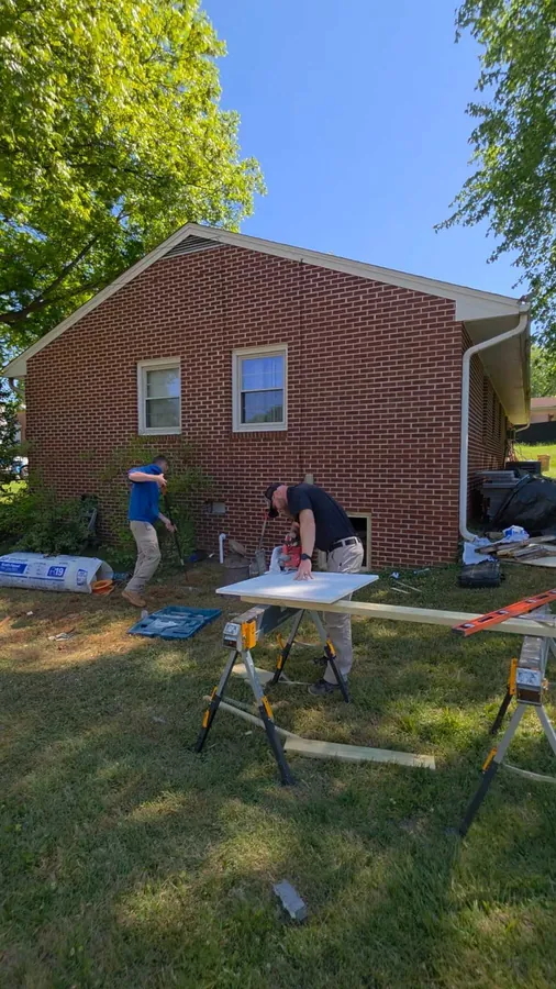 The Rozier Pest Control & Waterproofing crew working on a crawl space job outside a brick home, a work table set up on the lawn.