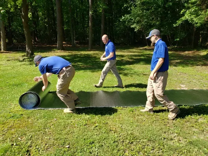 The Rozier Pest Control & Waterproofing crew unrolling drainage matting on a lawn before a crawl space install.