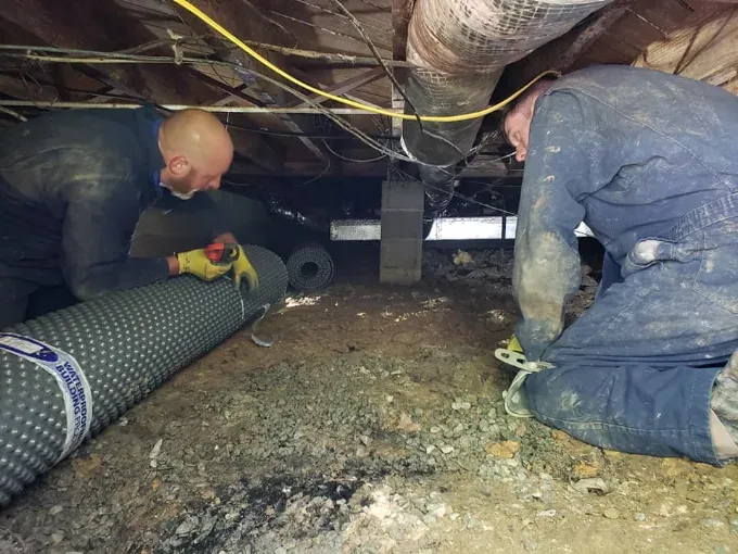 A Rozier Pest Control & Waterproofing crew installing crawl space drainage matting.