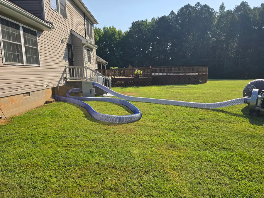 A Rozier Pest Control & Waterproofing crew installing a crawl space drying and ventilation system with large hoses and an exterior fan.