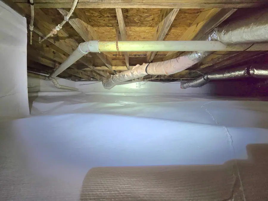 A clean crawl space with white vapor barrier on floor and walls.