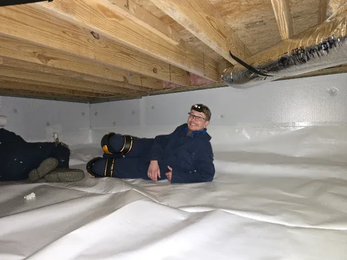 A Rozier Pest Control & Waterproofing crew member inside a crawl space during an encapsulation install, white liner on the walls and floor.