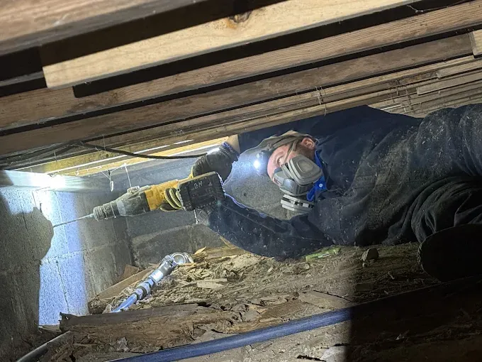 A Rozier Pest Control & Waterproofing technician drilling into a concrete block foundation wall during crawl space repair.
