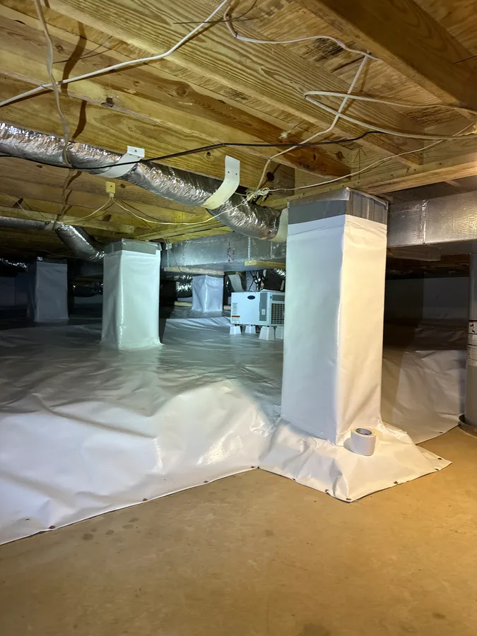 A white crawl space vapor barrier with sealed seams, installed by Rozier Pest Control & Waterproofing.