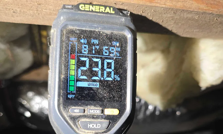A Rozier Pest Control & Waterproofing technician reading a digital moisture meter against crawl space framing.