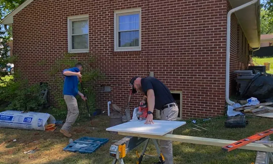 A Rozier Pest Control & Waterproofing crew preparing insulation board outside the crawl space access of a brick home.