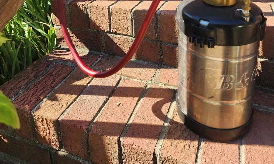 A Rozier Pest Control & Waterproofing sprayer on brick steps beside planters, ready for a targeted treatment.
