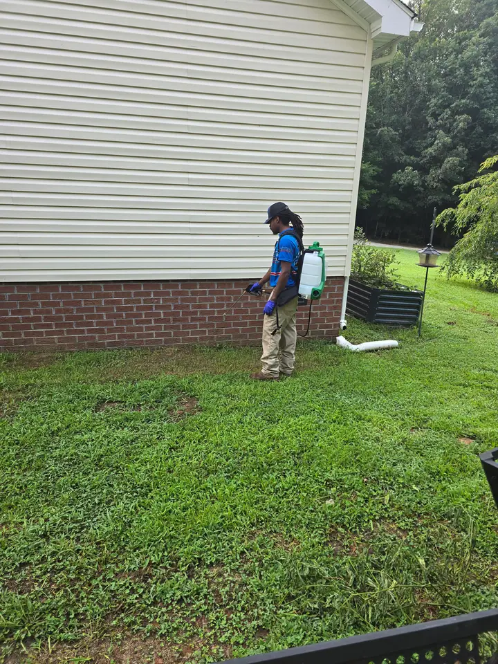 A Rozier Pest Control & Waterproofing technician applying a perimeter spray treatment to a home's foundation.