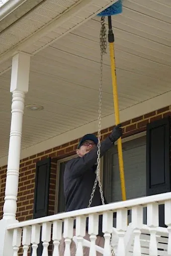 A Rozier Pest Control & Waterproofing technician treating an exterior soffit with a long pole sprayer.