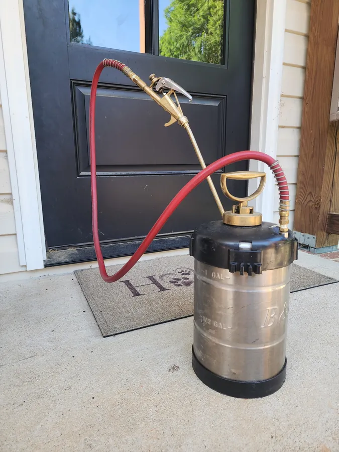 A Rozier Pest Control & Waterproofing sprayer in use along a residential foundation line.