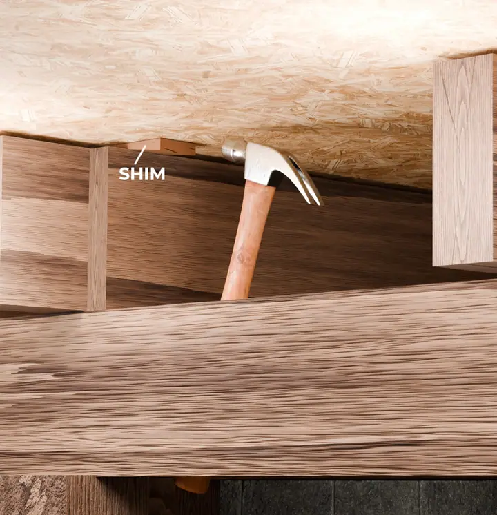 Illustration of a wooden shim being hammered into place between a floor joist and subfloor in a crawl.