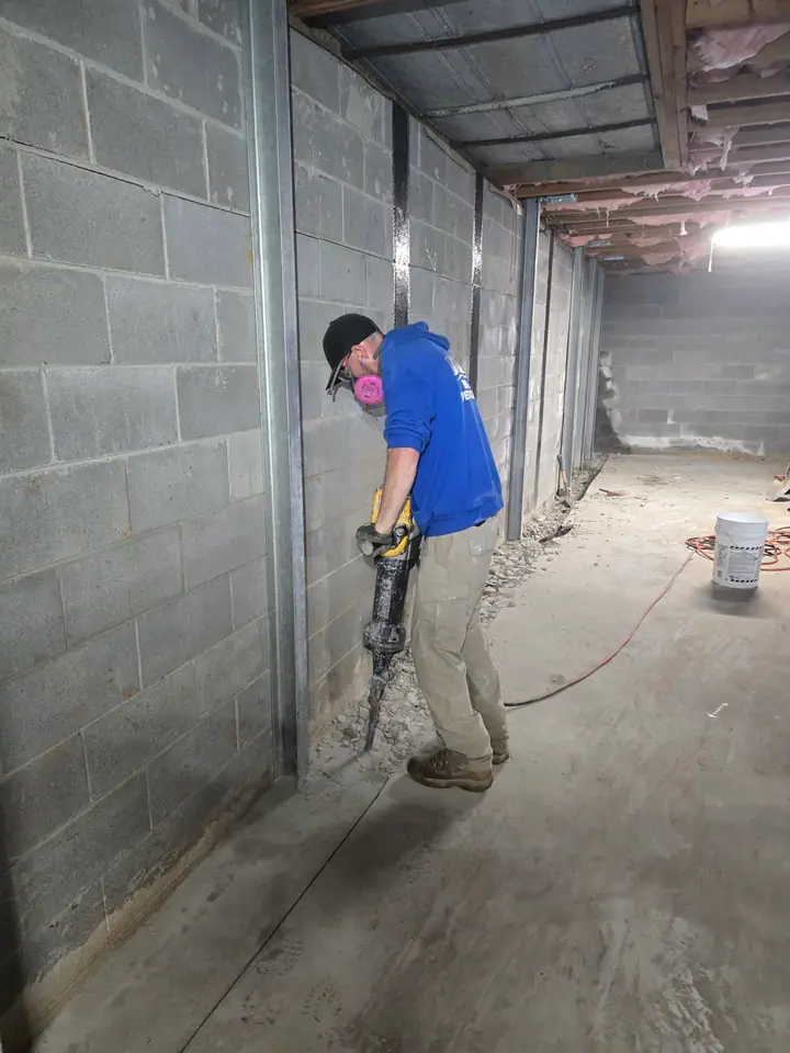 A Rozier Pest Control & Waterproofing technician working on a foundation wall with carbon fiber straps for stabilization.