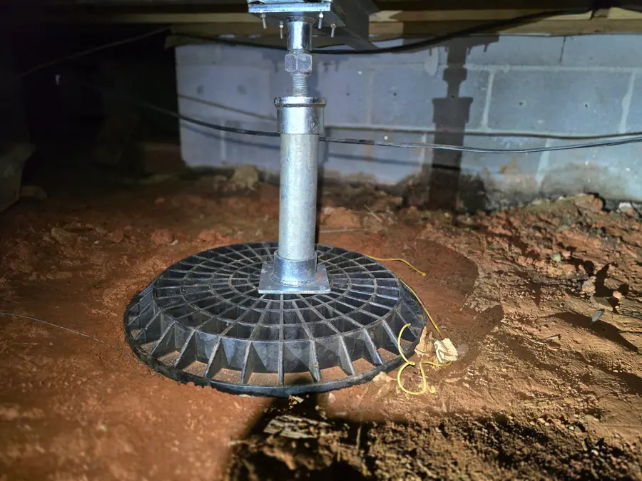 A Rozier Pest Control & Waterproofing crew installing an adjustable support jack in a dirt crawl space, providing structural support.