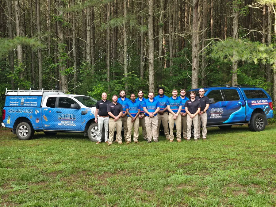 Rozier Pest Control & Waterproofing team members in front of two branded service trucks.