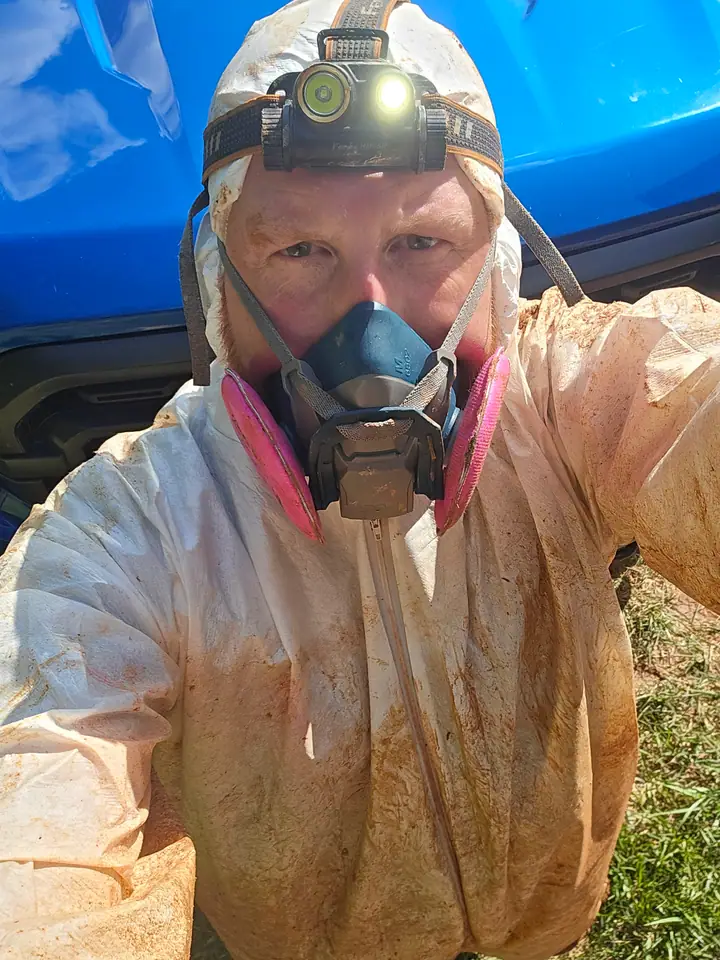 A Rozier Pest Control & Waterproofing team member in protective coveralls and a headlamp after a crawl space job.