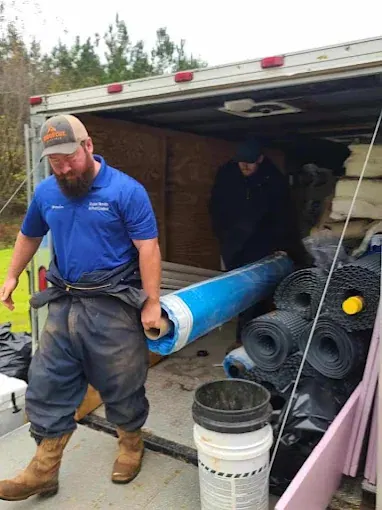 A Rozier Pest Control & Waterproofing crew member unloading vapor barrier rolls from the job trailer.