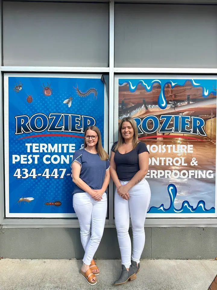 Two Rozier Pest Control & Waterproofing team members standing in front of the branded office windows.