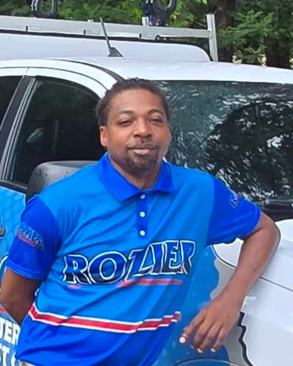 A Rozier Pest Control & Waterproofing team member in branded polo shirt leaning against a service truck.