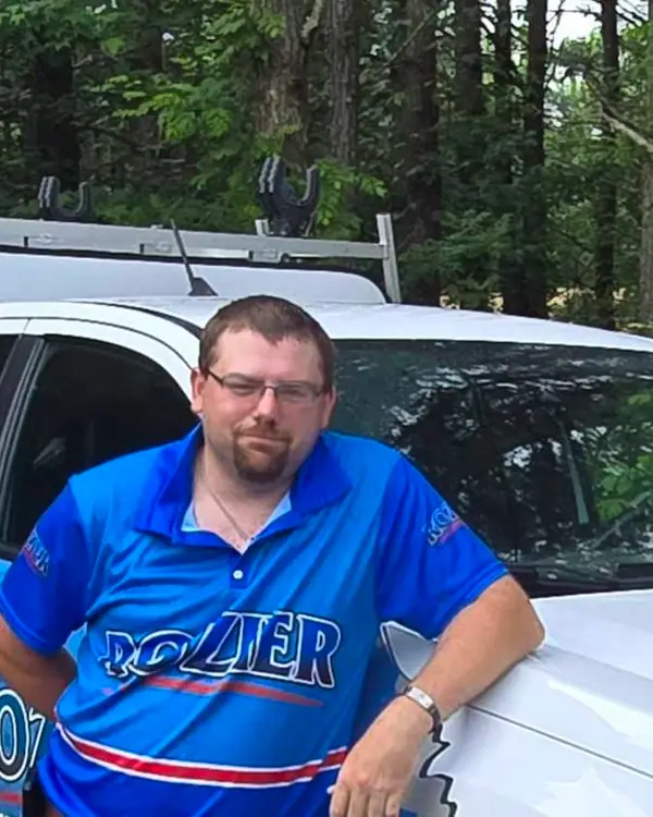 A Rozier Pest Control & Waterproofing team member in uniform leaning on a branded service vehicle.
