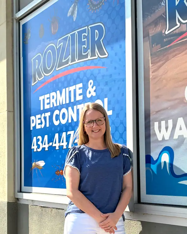 A Rozier Pest Control & Waterproofing team member smiling in front of the company office signage.
