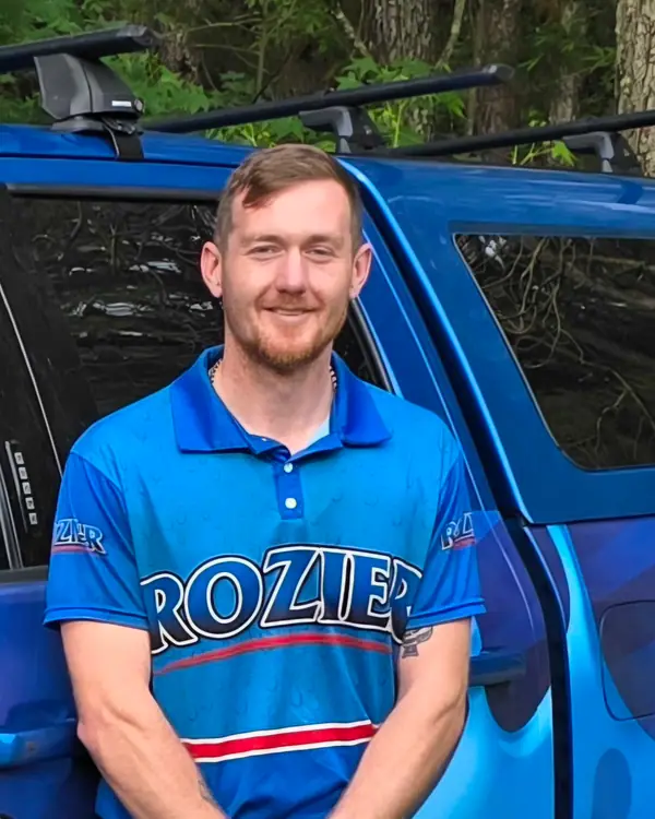 A Rozier Pest Control & Waterproofing team member smiling in branded uniform in front of a company service vehicle.