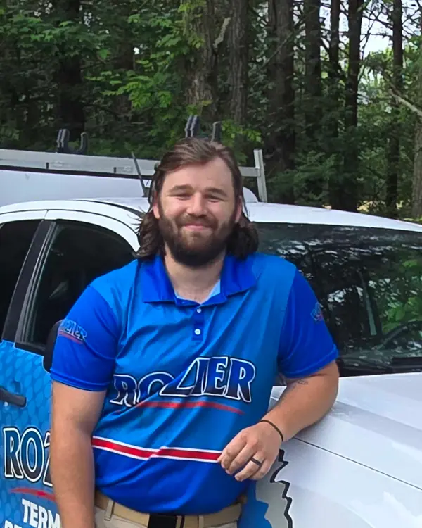 A Rozier Pest Control & Waterproofing technician smiling in uniform with a branded service vehicle.