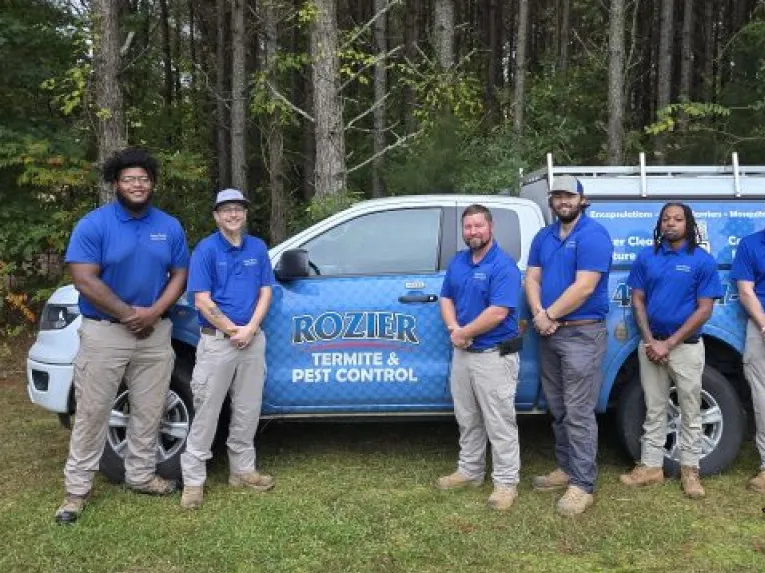 Six Rozier Pest Control & Waterproofing technicians standing in front of a branded service truck at the edge of the pines.