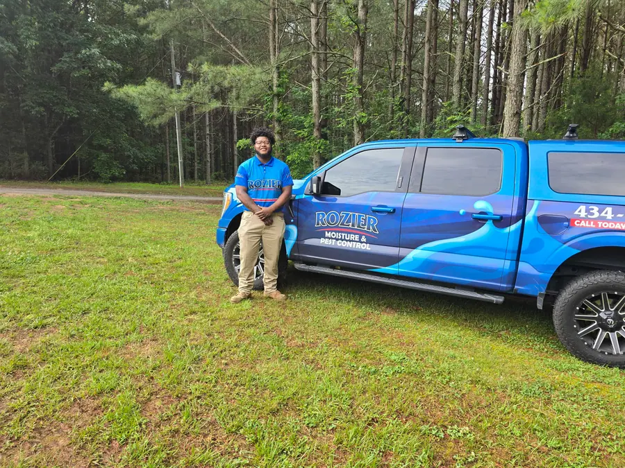 A Rozier Pest Control & Waterproofing team member in uniform standing proudly next to a branded service truck.