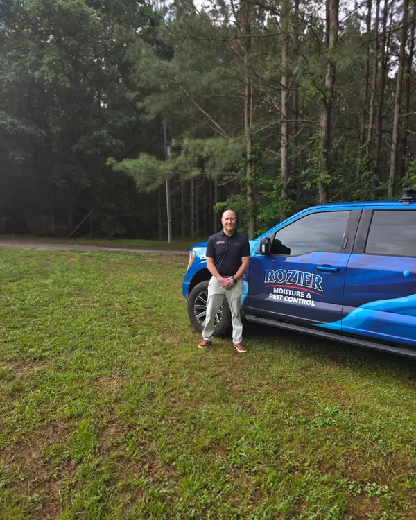 A Rozier Pest Control & Waterproofing team member standing beside a branded service truck.