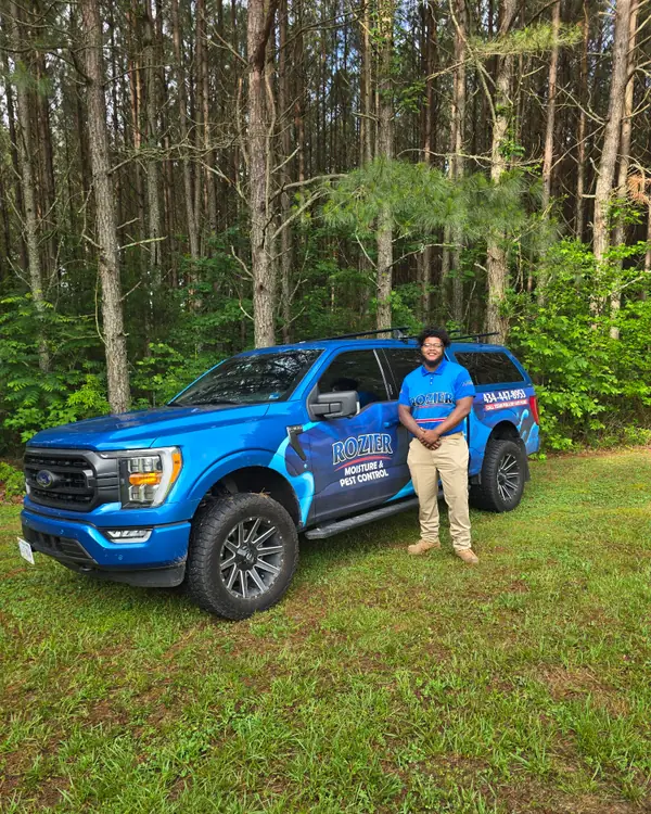 A Rozier Pest Control & Waterproofing technician standing beside a branded service truck.