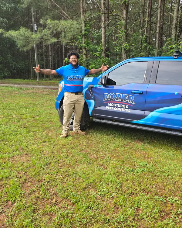 A Rozier Pest Control & Waterproofing technician beside a branded service truck, arms out in welcome.