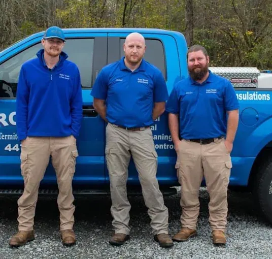 Three Rozier Pest Control & Waterproofing technicians standing in front of a company truck.