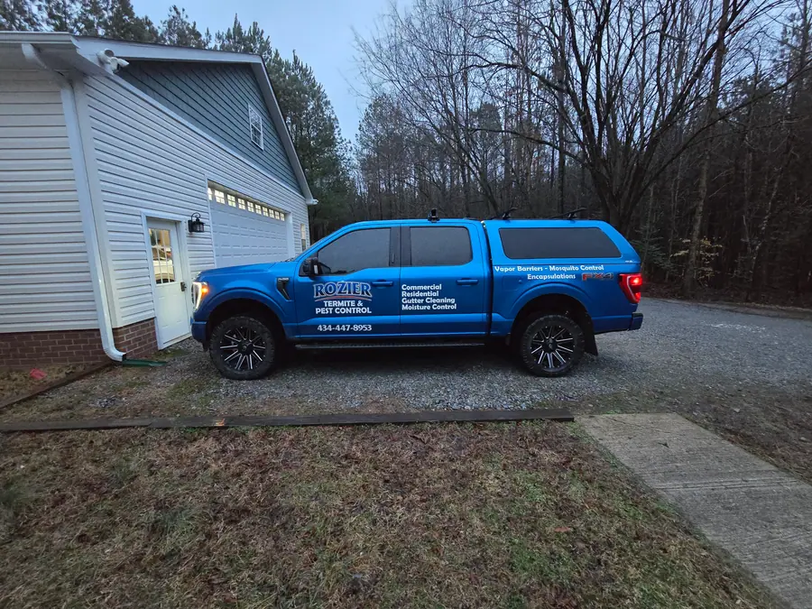 A Rozier Pest Control & Waterproofing branded blue service truck parked in front of a residential garage.