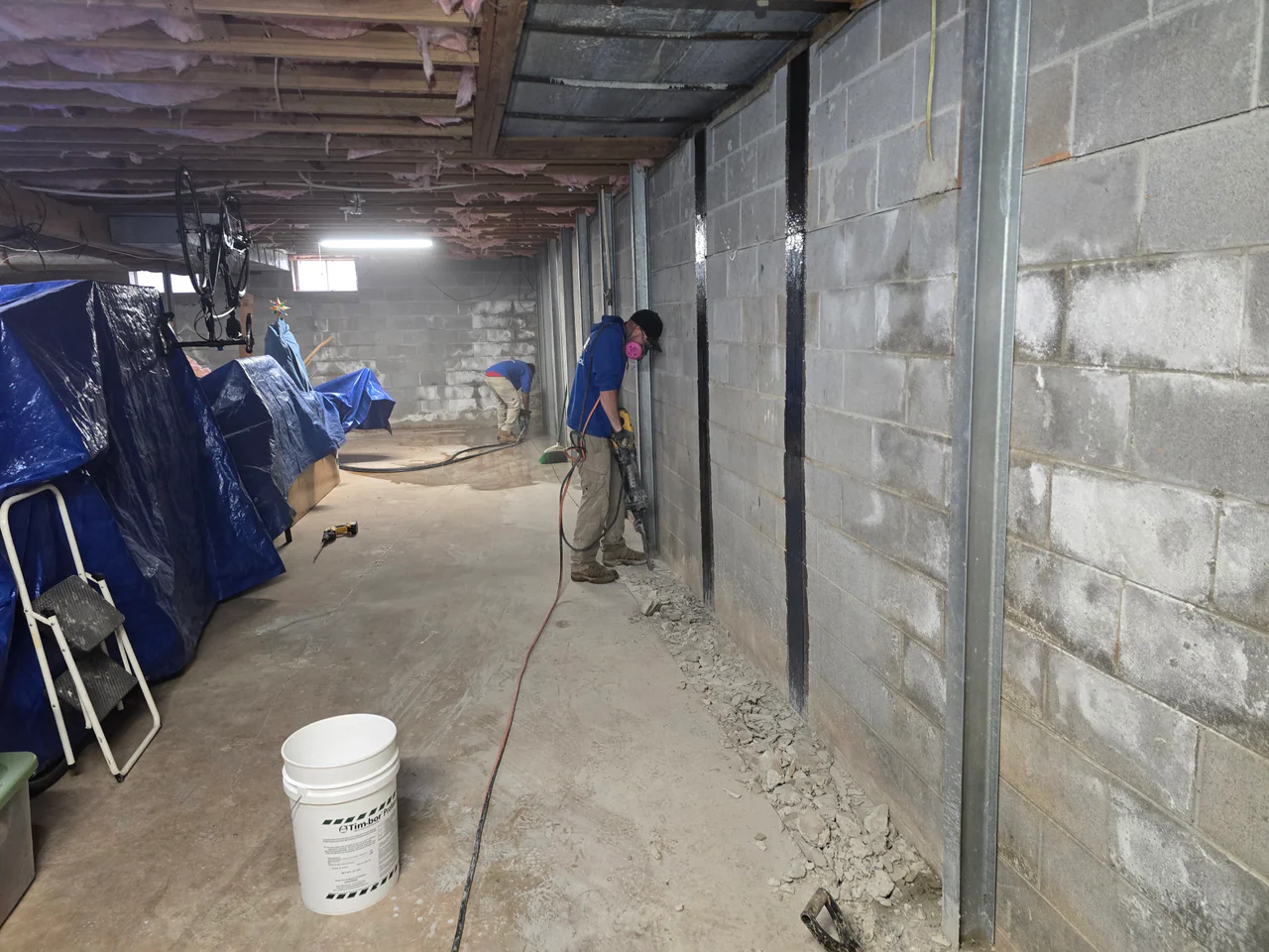 Rozier Pest Control & Waterproofing crew installing an interior drainage system in a basement to manage wet walls.